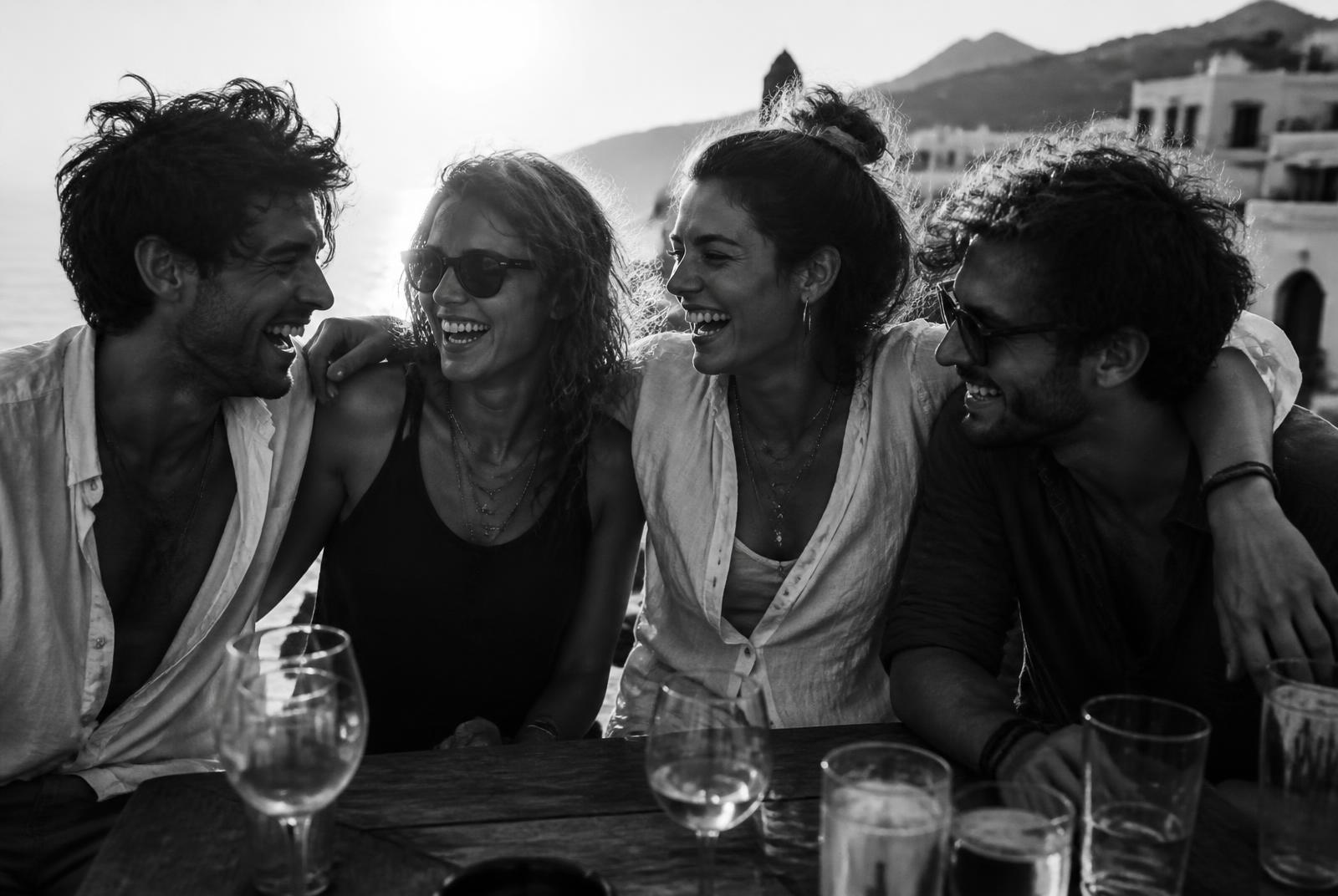 Bande de quatre amis qui rient en terrasse au coucher du soleil